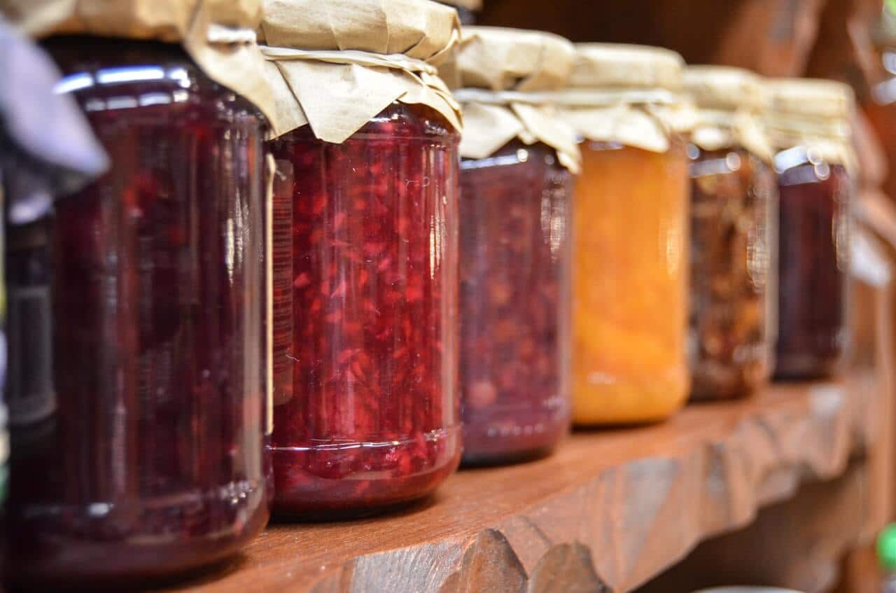 Glass mason jars filled with deep purple, red, crimson and yellow jams and jellies.