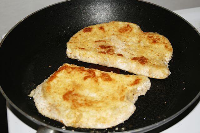 Two slices of giant puffball breaded and frying in a pan.